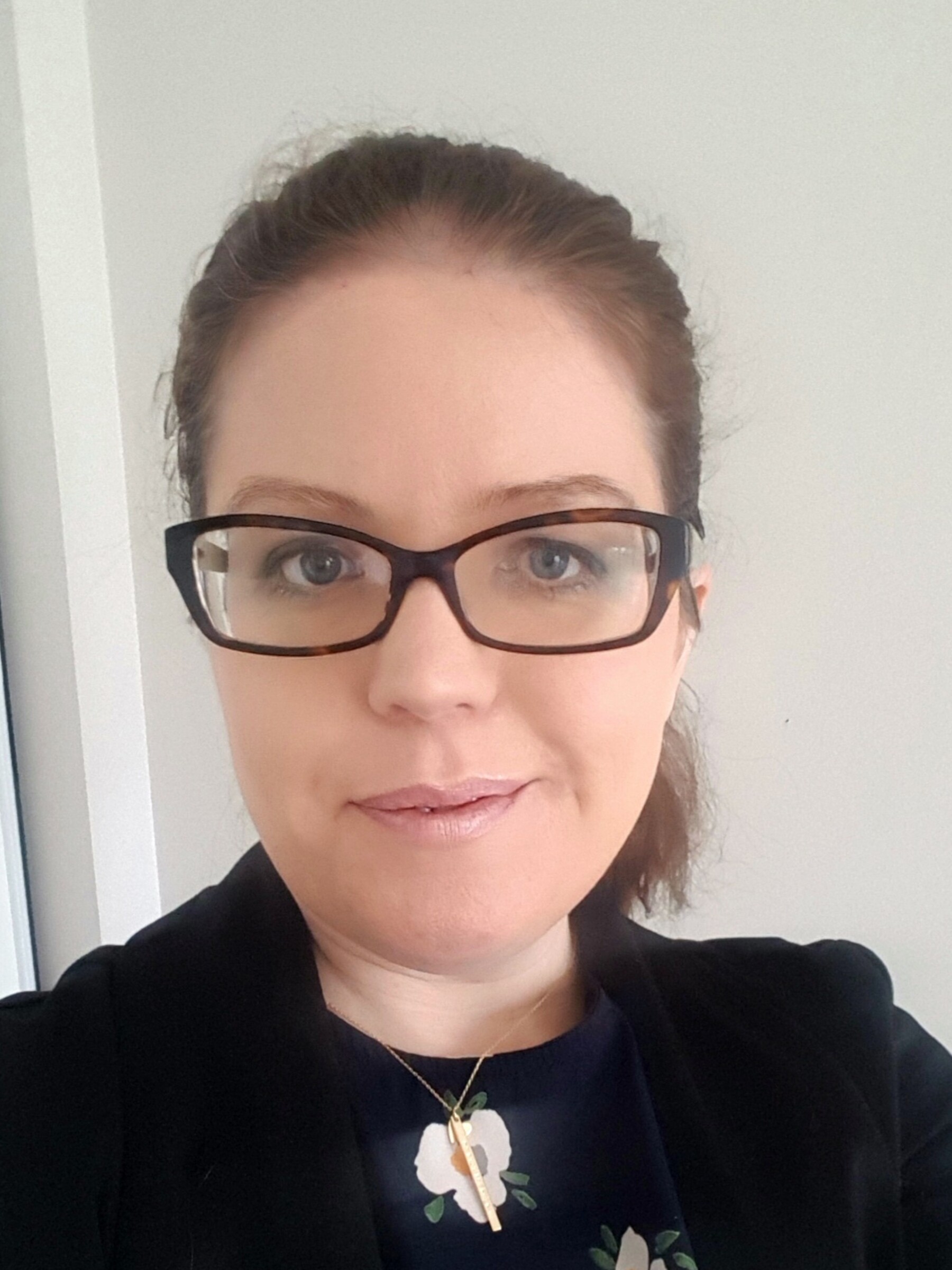 Photo of Dr. Avril Mansfield from the shoulders up. She has dark brown hair tied back in a pony tail. She is wearing dark, rectangular glasses. She is wearing a floral blouse with a black cardigan. She is smiling.