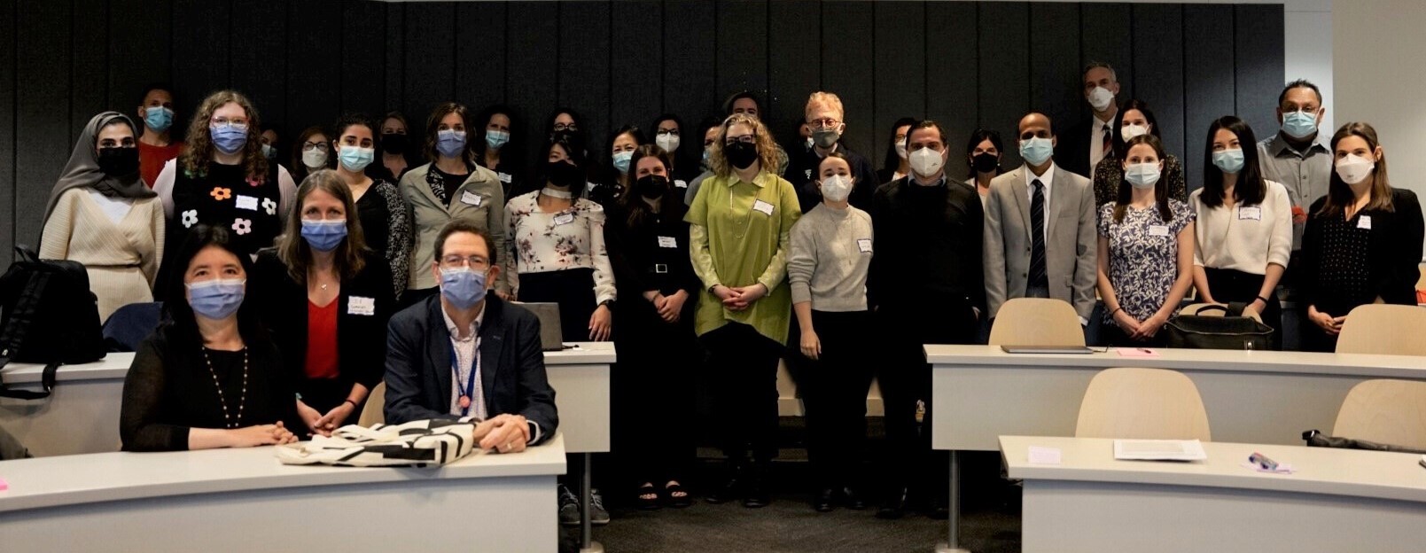 In-person attendees at the 2023 International Forum on COVID Rehabilitation Research pose for a photo in a lecture hall. They are all wearing masks.